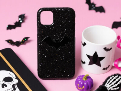 Halloween-themed black glitter phone case with bat pattern, paired with a star bat mug and a purple pumpkin ornament